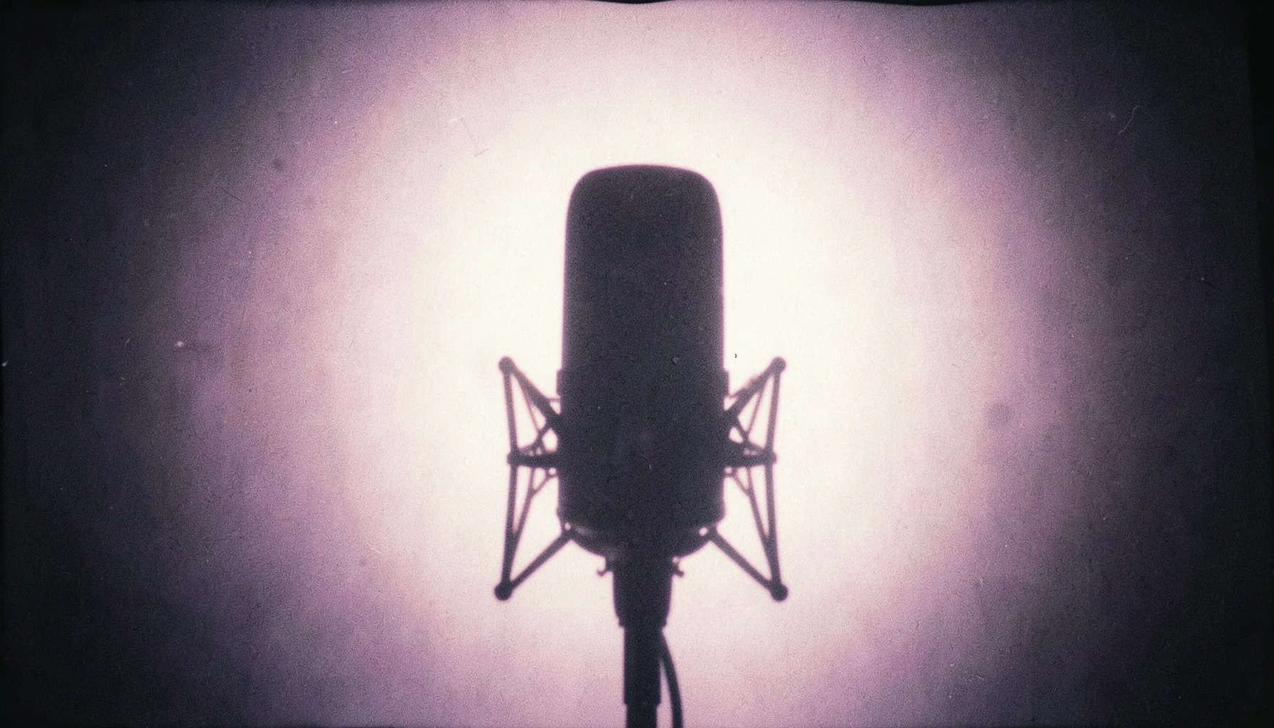 Yumuşak mor ve krem tonlarında soyut bir ışık huzmesi, bir stüdyo mikrofonunun silüetini arkadan aydınlatıyor; analog film greniyle dokulu, sakin ve manevi bir atmosfer.