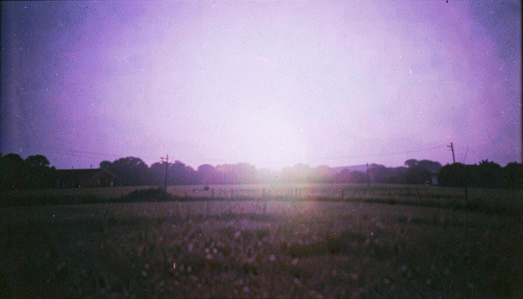Gece mavisi ve yumuşak beyaz ışık huzmeleriyle aydınlanan bir açık hava sahnesi; grenli analog fotoğraf.
