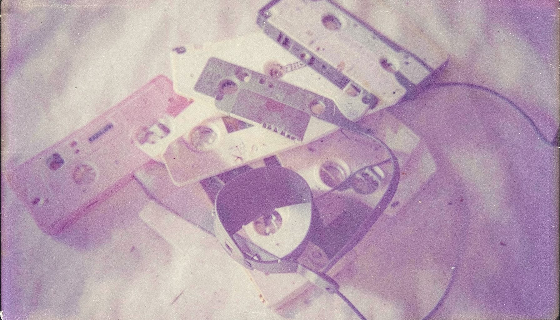 Pastel lavanta ve fildişi tonlarında, üst üste duran eski kaset bantları ve bir kulaklık, nostaljik analog his.