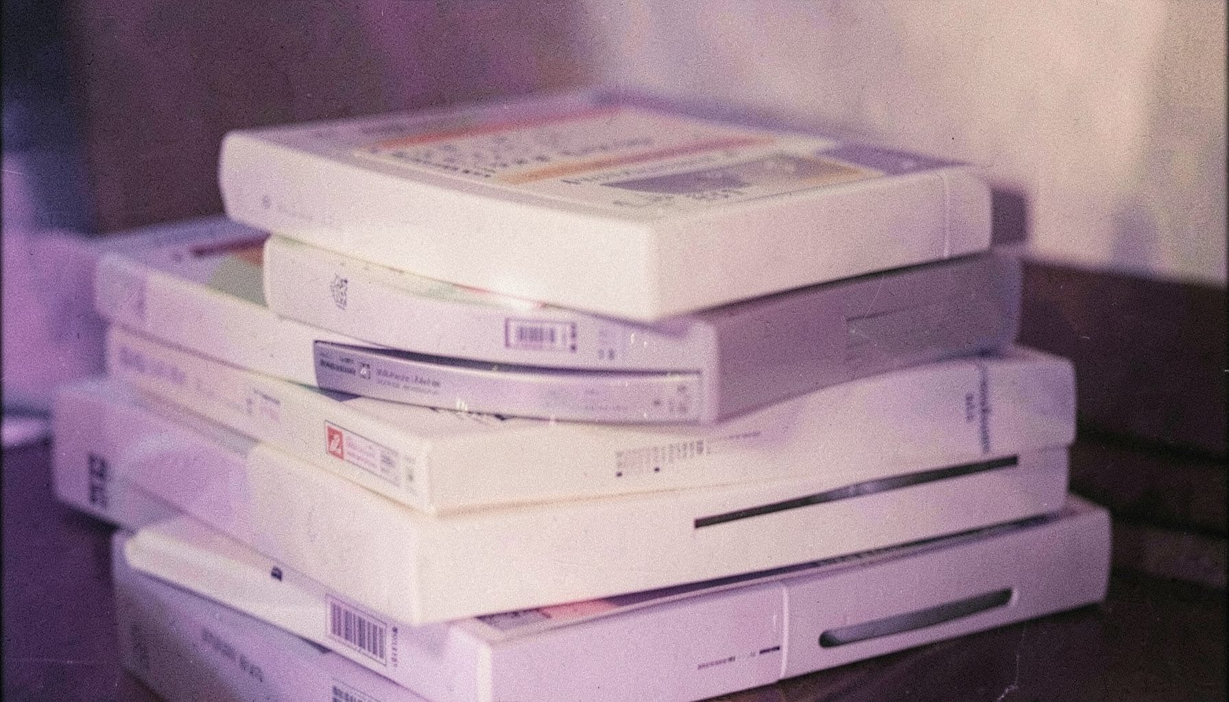 Açık bej ve yumuşak mor tonlarında, üst üste dizilmiş DVD kutuları; yanlarından hafif ışık sızıyor, film greniyle sıcak ve dokulu bir his.